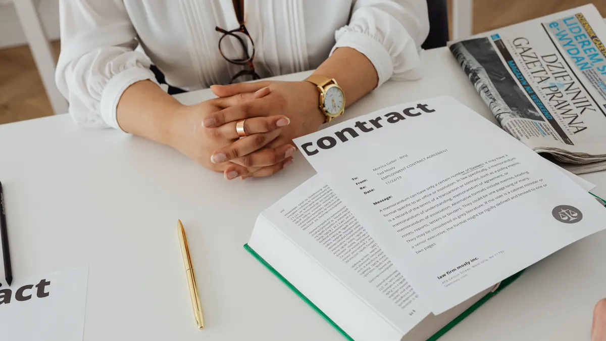 Femme d'affaires à un bureau examinant un contrat posé sur un livre, avec documents juridiques et journal.