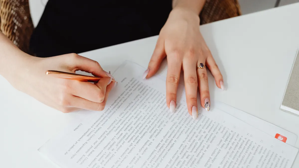 Une femme signe un document avec un stylo sur un bureau, mettant l'accent sur les mains et l'écriture.